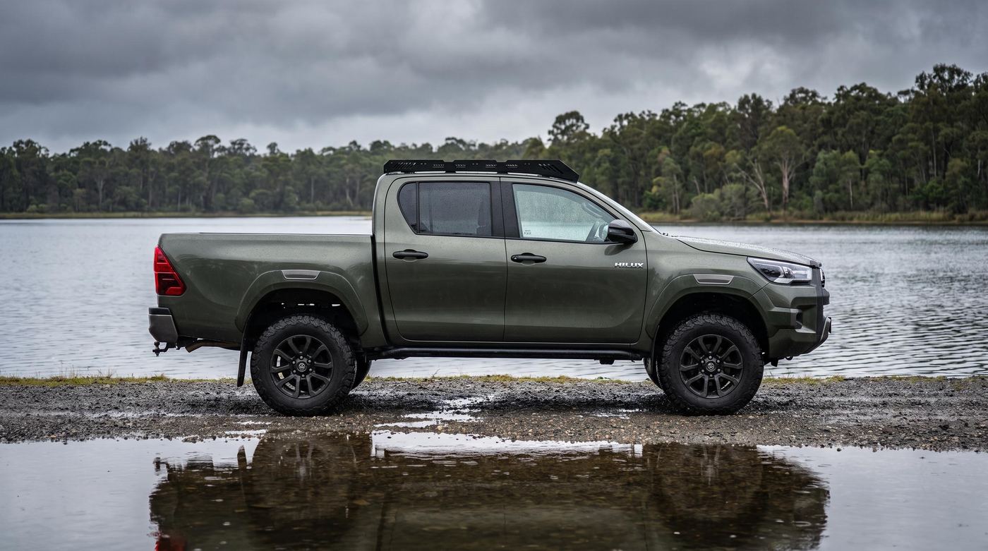 Green Toyota Hilux double cab with a low-profile steel platform roof rack on a lake shore