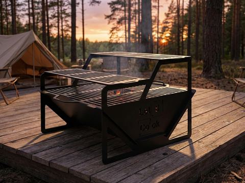 Black flat-pack steel fire pit with grill grates on a wooden deck at a campsite