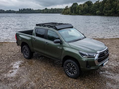 Green Toyota Hilux double cab with a low-profile black platform roof rack on a lake shore